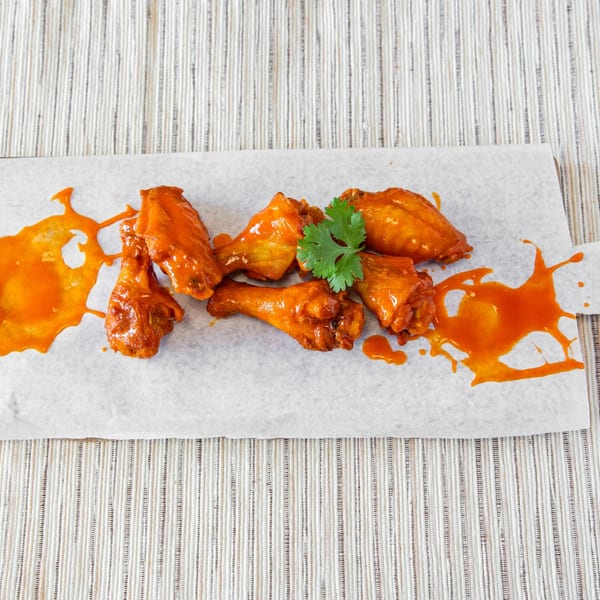 Six buffalo chicken wings with cilantro garnish and sauce splatters on a white paper-lined board.