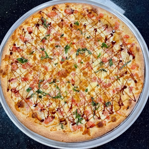 Whole pizza with cheese, diced tomatoes, basil, and balsamic glaze on a metal pan.