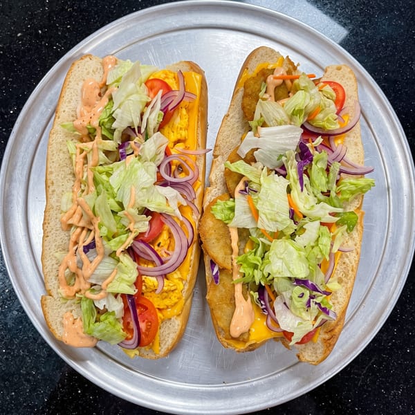 Two hearty subs filled with fried protein, melted cheese, lettuce, tomatoes, onions, and a creamy sauce.