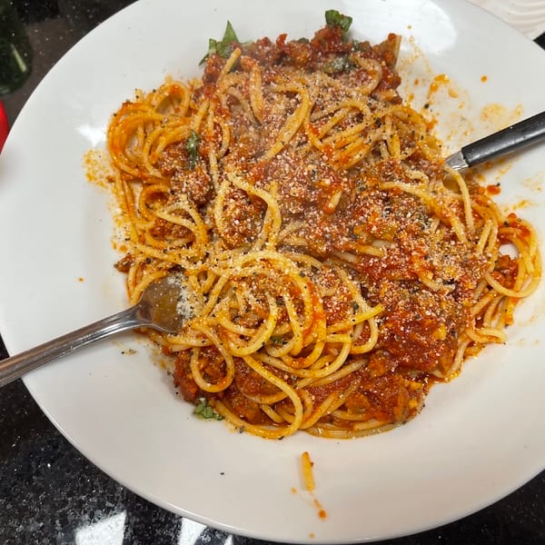 Spaghetti with rich red sauce, grated cheese, and herbs on a white plate with a fork and knife.