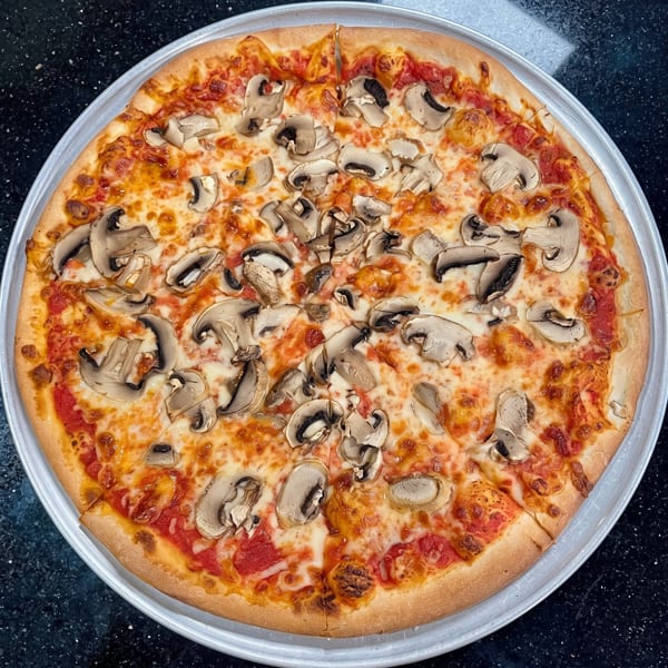 Whole mushroom pizza with melted cheese and red sauce on a round metal pan.