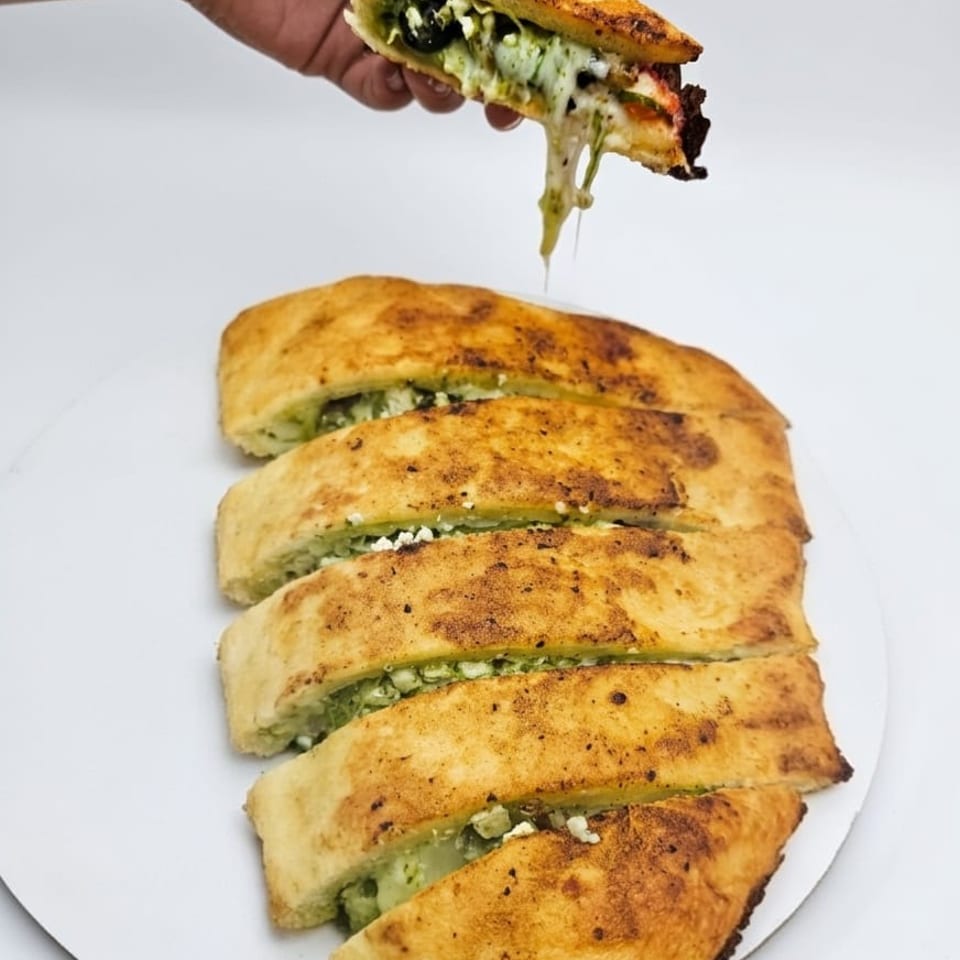 Hand holding a cheesy pesto breadstick with melted cheese stretching, above a platter of sliced breadsticks.