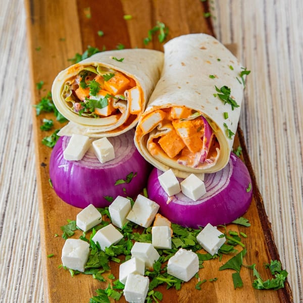Two paneer wraps with red onions, feta cheese, and cilantro on a wooden board.