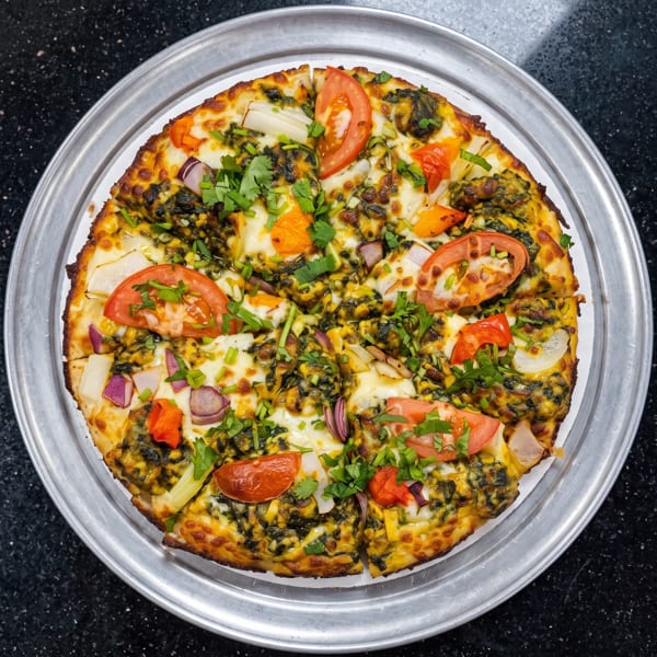 A colorful pizza with pesto, melted cheese, tomatoes, onions, and fresh cilantro on a metal tray.