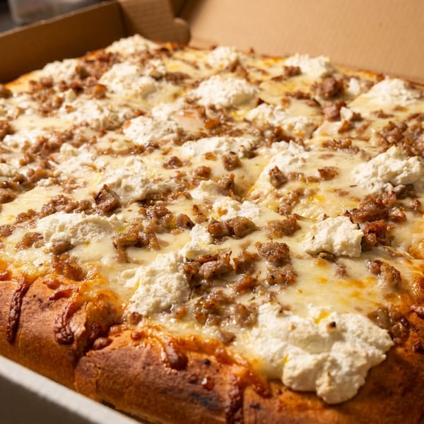 Square pizza with sausage, mozzarella, and ricotta cheese in a cardboard box.